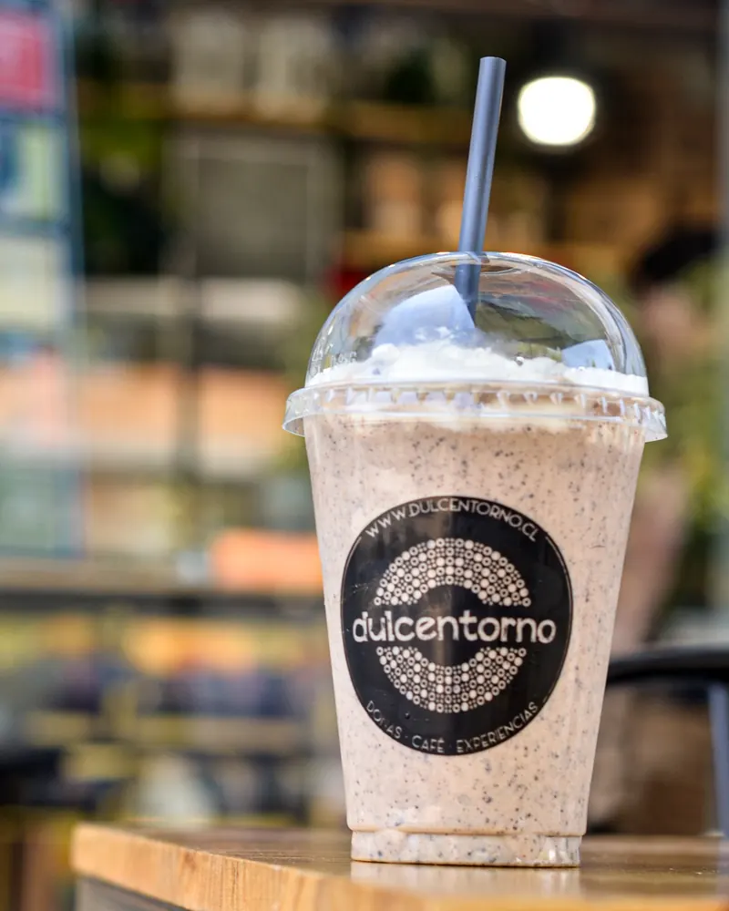 Batido con trozos de galleta y crema en vaso Dulcentorno, sobre una mesa de madera