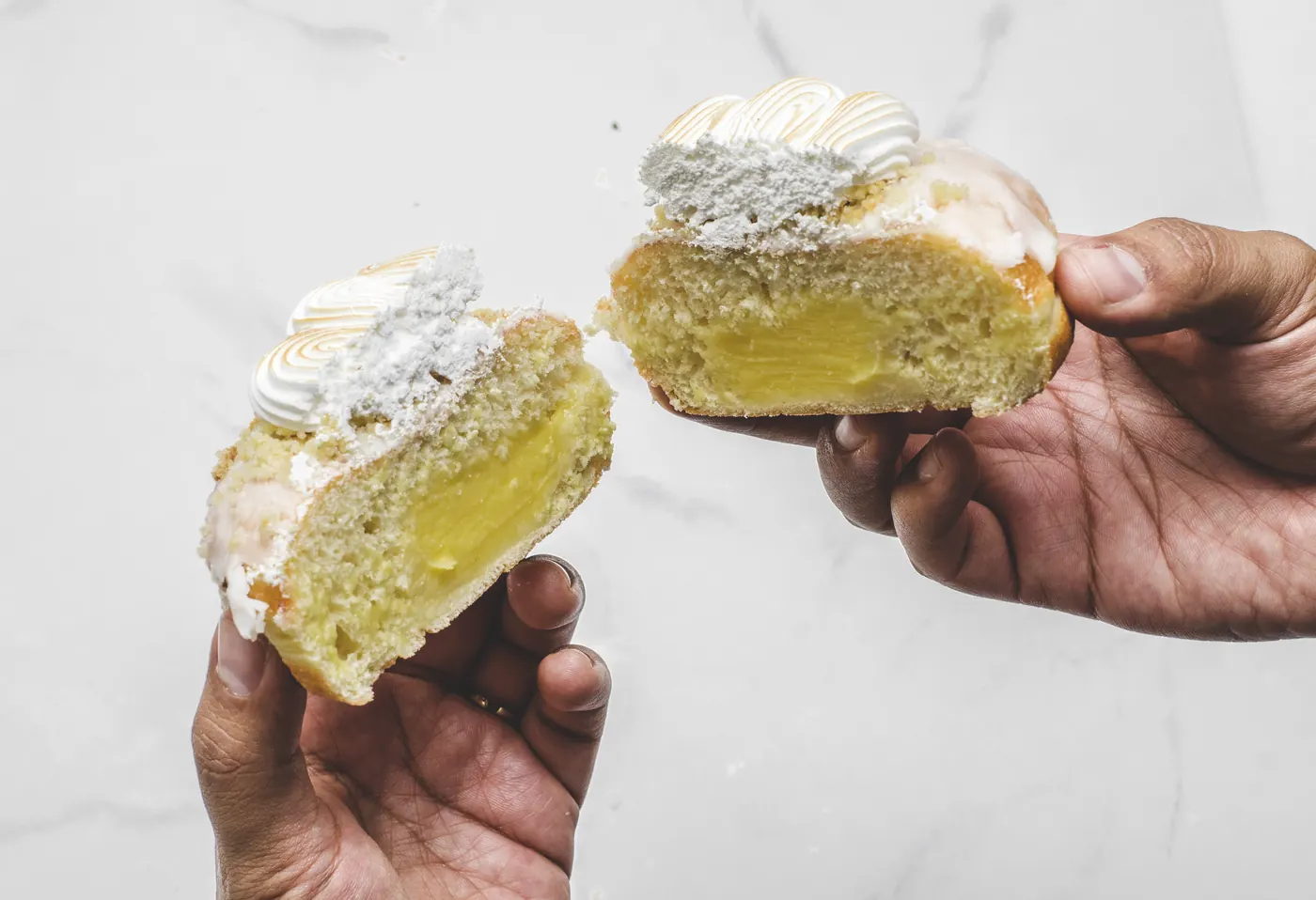 Dos manos comparten una dona partida por la mitad, rellena de crema pastelera y con merengue