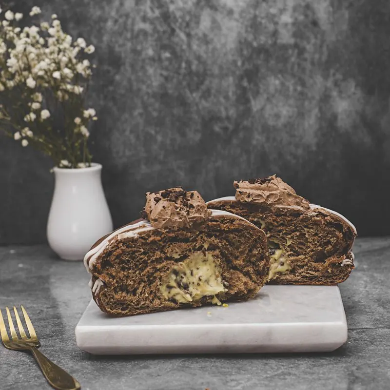 Dona de chocolate partida en dos sobre mármol, con relleno de crema pastelera