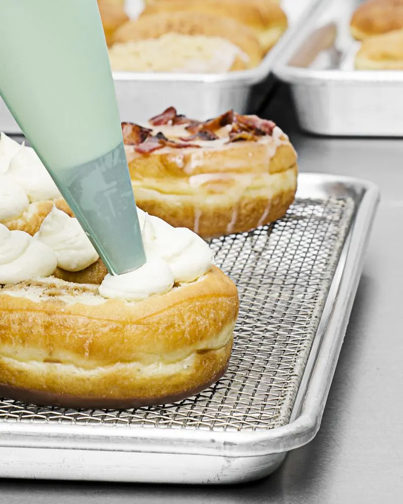Manga pastelera rellenando con crema una dona sobre la rejilla